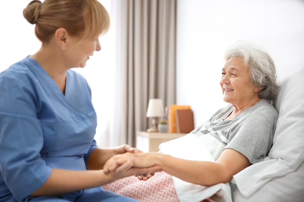 Elderly woman in bed smiling at care worker